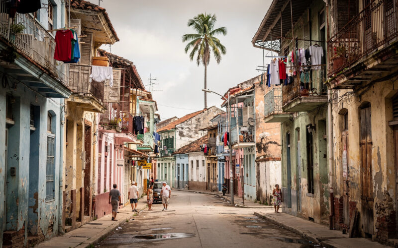 Wąska ulica w Centro Habana z zabytkową zabudową kolonialną, odpadającym tynkiem i balkonami, lokalni mieszkańcy spacerują po chodniku