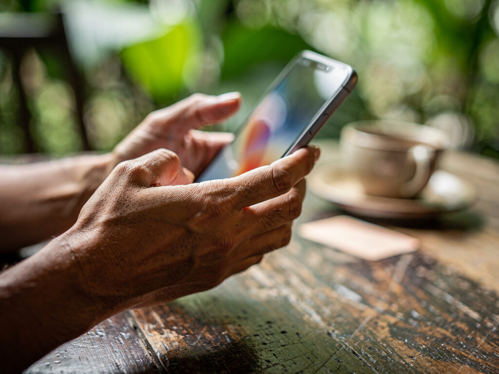 Dłonie trzymające smartfon nad drewnianym stolikiem w kawiarni, obok nieczytelna karta dostępu do internetu, miękkie naturalne światło